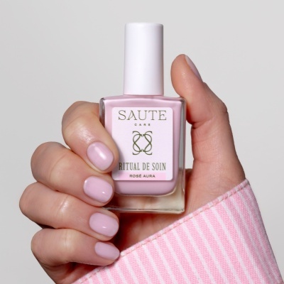 Frasco de verniz de unhas rosa segurado por mão feminina com unhas da mesma cor.