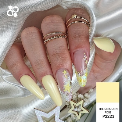 Unhas em amarelo pastel com decoração de estrelas e brilho, segurando estrelas decorativas sobre tecido bege claro.