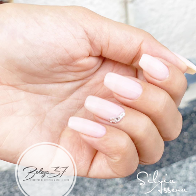 Mão com unhas artificiais rosa claro e detalhes de cristais prateados