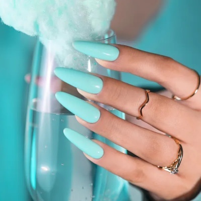 Mão com unhas azuis segurando copo de vidro com espuma