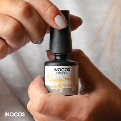 Mãos segurando frasco preto de verniz gel INOCOS com texto 'Parreirinha de Alfama'.