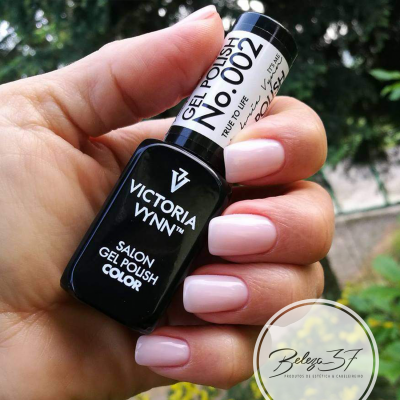 Verniz gel preto Victoria Vynn com unhas pintadas rosa claro segurando o frasco