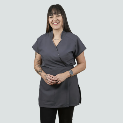 Mulher com túnica cinza escura e calças pretas num fundo cinzento claro