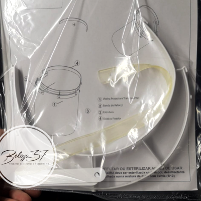 Protetor facial transparente com peças brancas e instruções em português, embalado em saco plástico