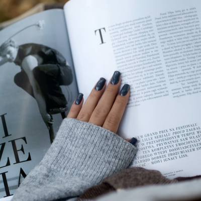 Mão feminina com unhas cinza escuro segurando livro aberto