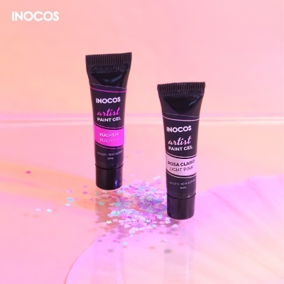 Dois tubos pretos de gel para pintura INOCOS com rótulos rosa e branco sobre superfície rosa com confetes prateados