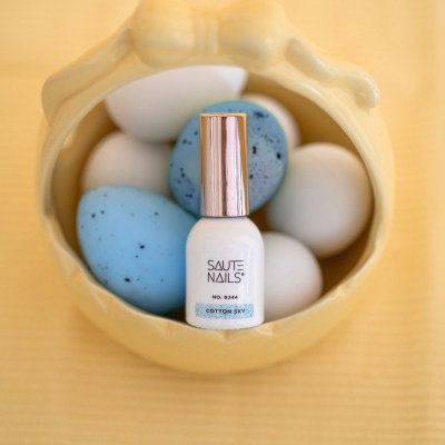Verniz de unhas SAUTE NAILS cor COTTON SKY dentro de recipiente amarelo com ovos decorativos azuis e brancos