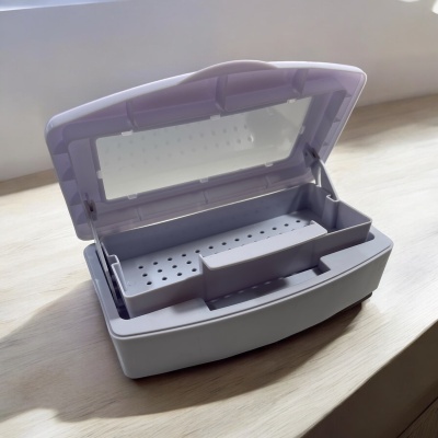 Caixa plástica cinzenta com tampa translúcida roxa aberta, interior com divisórias