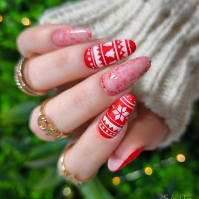 Unhas vermelhas e brancas com padrão natalício e efeito marmoreado, mão com anéis dourados