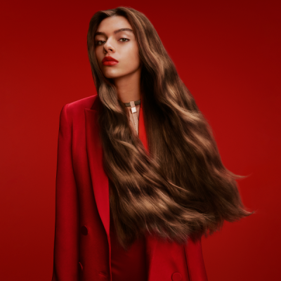 Mulher com cabelo longo ondulado e blazer vermelho numa parede vermelha
