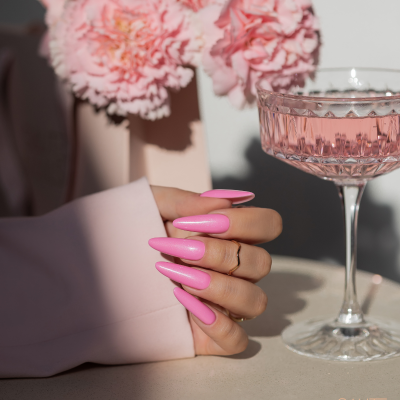 Mão com unhas longas cor-de-rosa junto a taça de vidro e flores cor-de-rosa