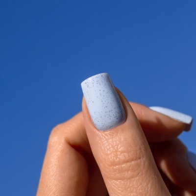 Unha com verniz azul claro com manchas pretas e fundo de céu azul