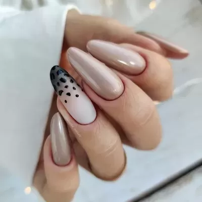 Unhas largas alongadas em tons de bege com uma unha estampada com manchas pretas.
