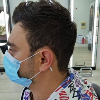 Homem de perfil usando máscara azul e camisola com capuz estampada num salão de cabeleireiro