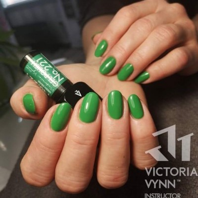Mãos femininas com unhas verdes brilhantes segurando um frasco de verniz de unhas verde