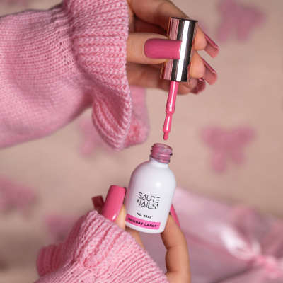 Verniz de unhas cor-de-rosa Holiday Candy da SAUTE NAILS junto a mãos com camisola cor-de-rosa