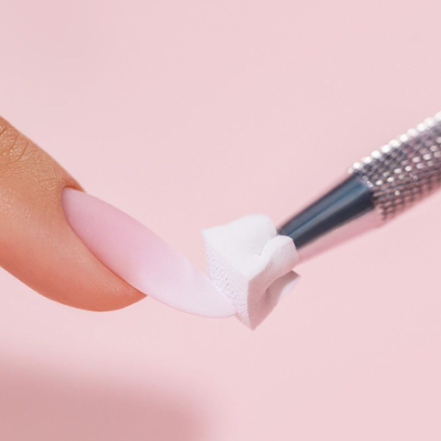 Unha rosa clara mate com ferramenta metálica a aplicar pequeno cubo branco sobre ela