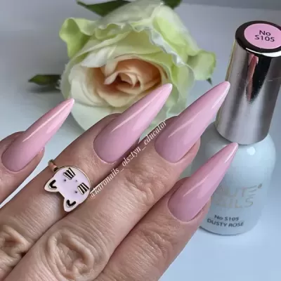 Unhas compridas cor rosa claro com anel de gato e garrafa de verniz