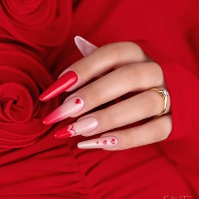 Mão com unhas decoradas em padrão vermelho e nude com corações e anel dourado