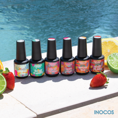 Seis frascos de verniz gel INOCOS com rótulos coloridos e tampas pretas ao lado de frutas junto a uma piscina