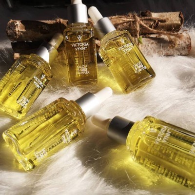 Frascos de óleo amarelo VICTORIA VYNN com conta-gotas sobre superfície branca felpuda