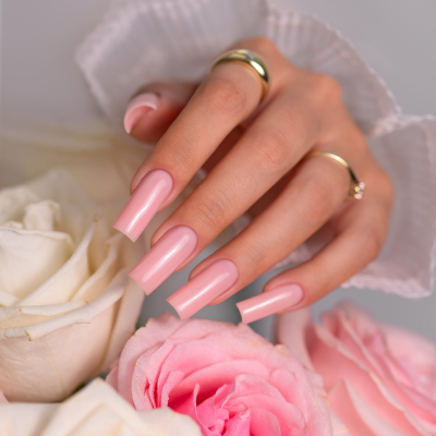 Mão com unhas longas e rosa claro segurando rosas brancas e rosas, anéis dourados visíveis, texto SAUTE NAILS