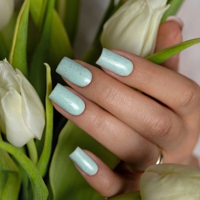 Unhas pintadas de azul claro com manchas escuras segurando flores brancas