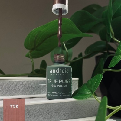 Frasco de verniz gel castanho escuro Andreia True Pure junto a folhas verdes