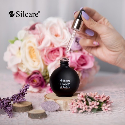 Frasco preto de óleo serum para mãos e unhas Silcare com conta-gotas e flores em fundo desfocado