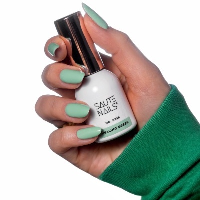Mão feminina segurando frasco de verniz verde da marca SAUTE NAILS.