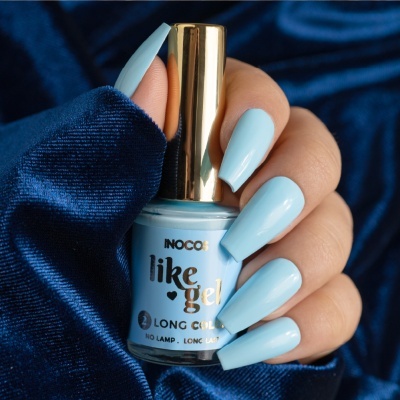 Frasco de verniz de unhas azul claro com texto, mão com unhas pintadas da mesma cor e fundo azul veludo.