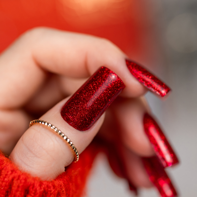 Unha com verniz glitter vermelho e anel dourado em mão com suéter vermelho