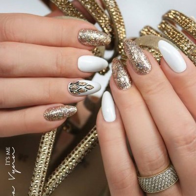 Mãos com unhas decoradas em branco e glitter dourado segurando acessório dourado com pedras e anel brilhante