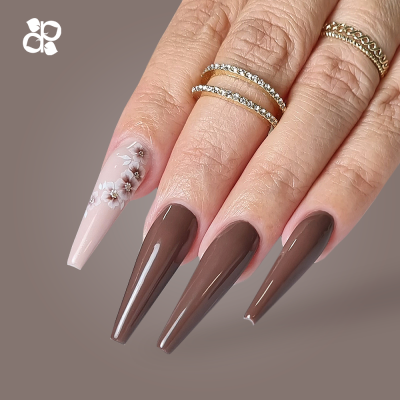 Mão com unhas compridas castanhas e rosa claro com flores, e três anéis dourados