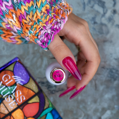 Unhas pintadas de rosa vibrante com frasco de verniz no centro e suéter colorido em fundo cinzento