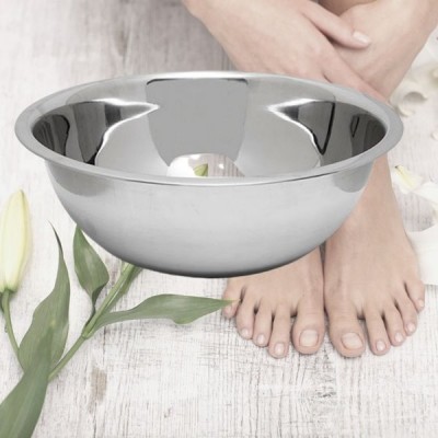 Tigela de aço inoxidável prateada brilhante junto a pés descalços e flor branca em chão claro