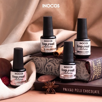 Frascos de verniz de unhas INOCOS top coat natura sobre toalha bege, caixa decorativa, livros e especiarias naturais