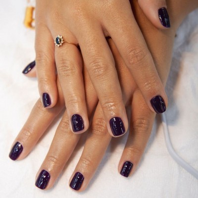Mãos femininas com unhas pintadas de verniz roxo escuro brilhante e anel dourado com pedra azul