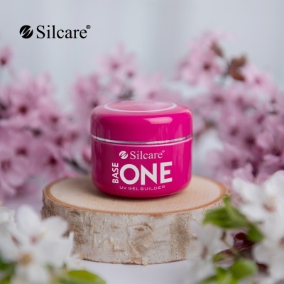 Frasco rosa de gel UV para unhas da marca Silcare, sobre tronco de madeira com flores ao fundo