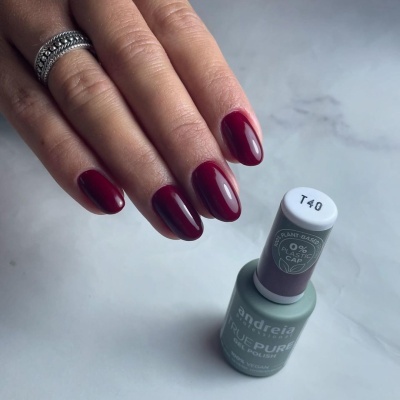 Mão com unhas pintadas de verniz bordeaux brilhante e frasco de verniz andreia TRUE PURE COLOR T40