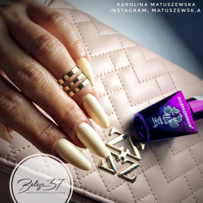 Mão feminina com unhas bege fosco e anel dourado sobre mala rosa matelassê e frasco roxo