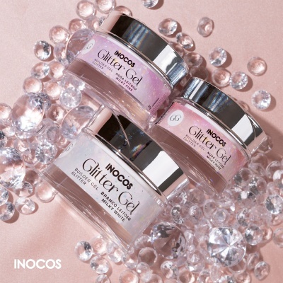 Três potes de gel de brilho com glitter da INOCOS em fundo rosa com brilhantes