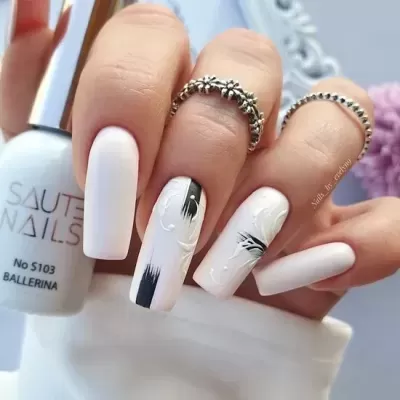 Unhas brancas mate com detalhes pretos e florais, frasco de verniz branco e anéis prateados