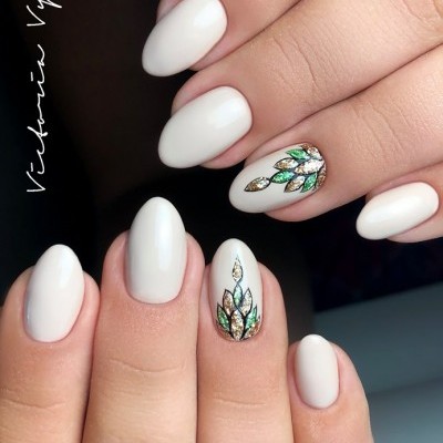 Unhas pintadas de branco com decoração de folhas em verde, dourado e prateado