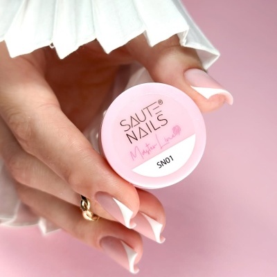 Frasco pequeno rosa de produto para unhas segurado por mão com unhas francesas sobre fundo rosa