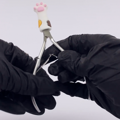 Alicate de cutícula com cabo decorado com pata de gato e mãos com luvas pretas a limar unhas.