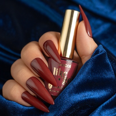 Mão feminina com unhas castanho avermelhado segurando frasco de verniz em tecido azul