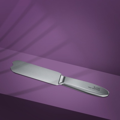 Espátula de cozinha de aço inox soldada com inscrição no cabo sobre fundo roxo.