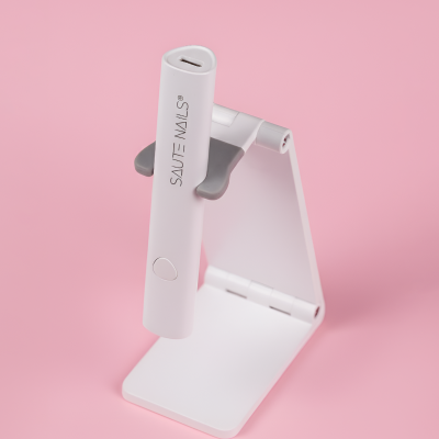 Dispositivo branco SAUTE NAILS® em suporte dobrável branco em fundo rosa