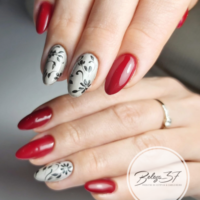 Unhas pintadas com verniz vermelho e branco com padrão floral preto.